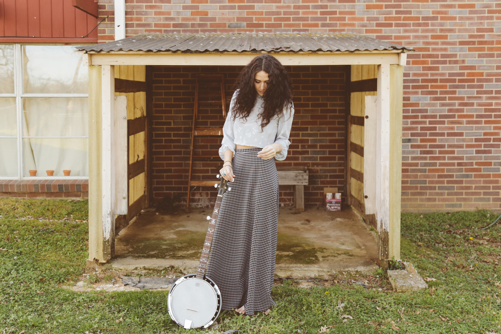 Lauren in front of a small barn with her banjo