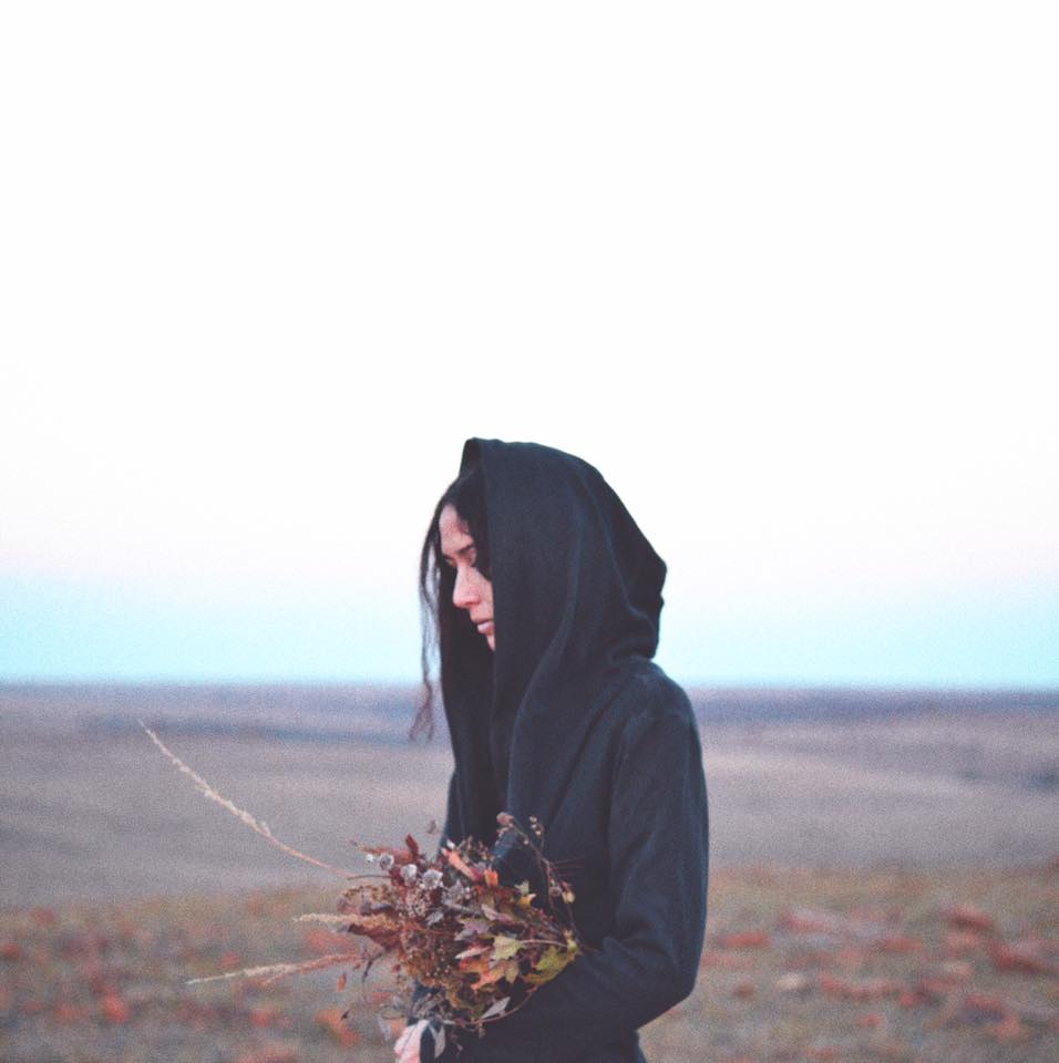 Lauren standing in a field with her hood on her head while holding flowers